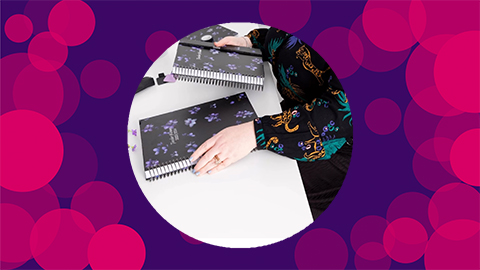 A purple background with pink circles on with an image of the Midnight Petals journals and an arm in the middle of the canvas.